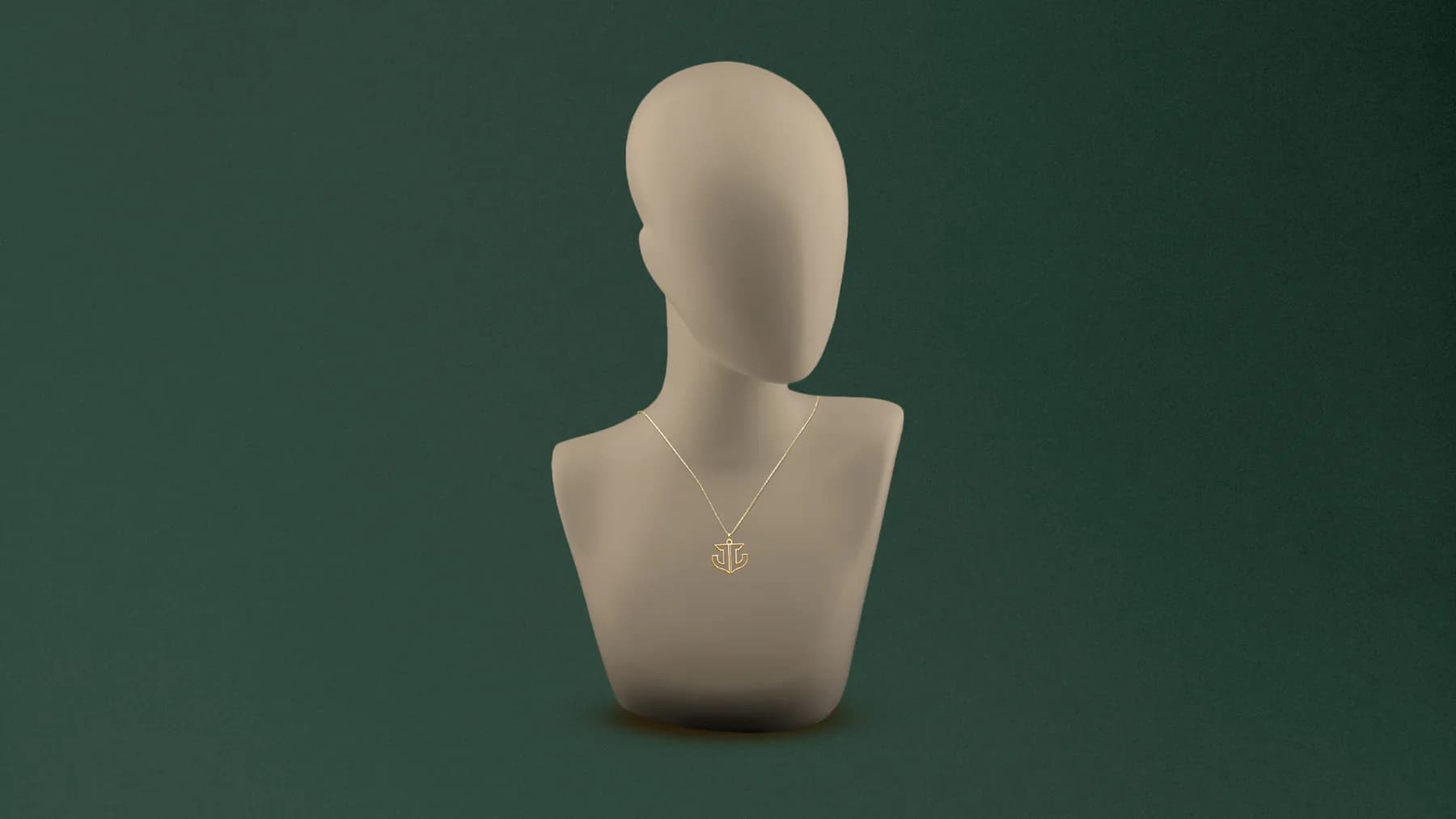 Busto de exposição bege sobre fundo verde escuro, com uma corrente fina de ouro e o pingente do símbolo da Jussara Joias